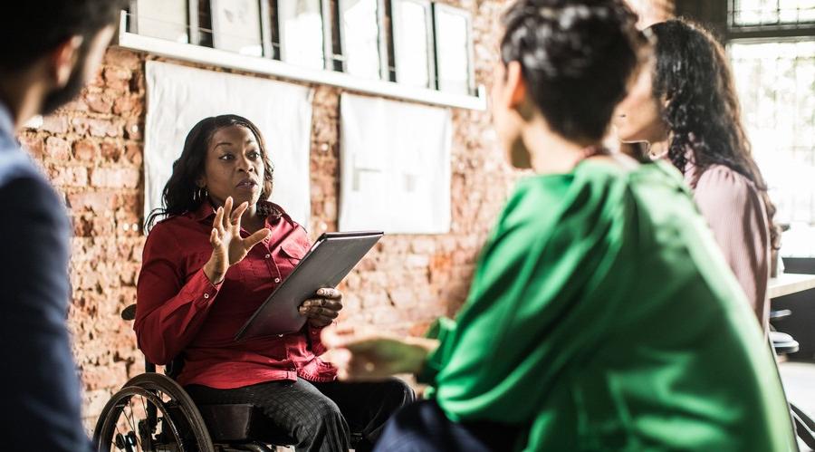 Person in a wheelchair holding a tablet is speaking to two colleagues